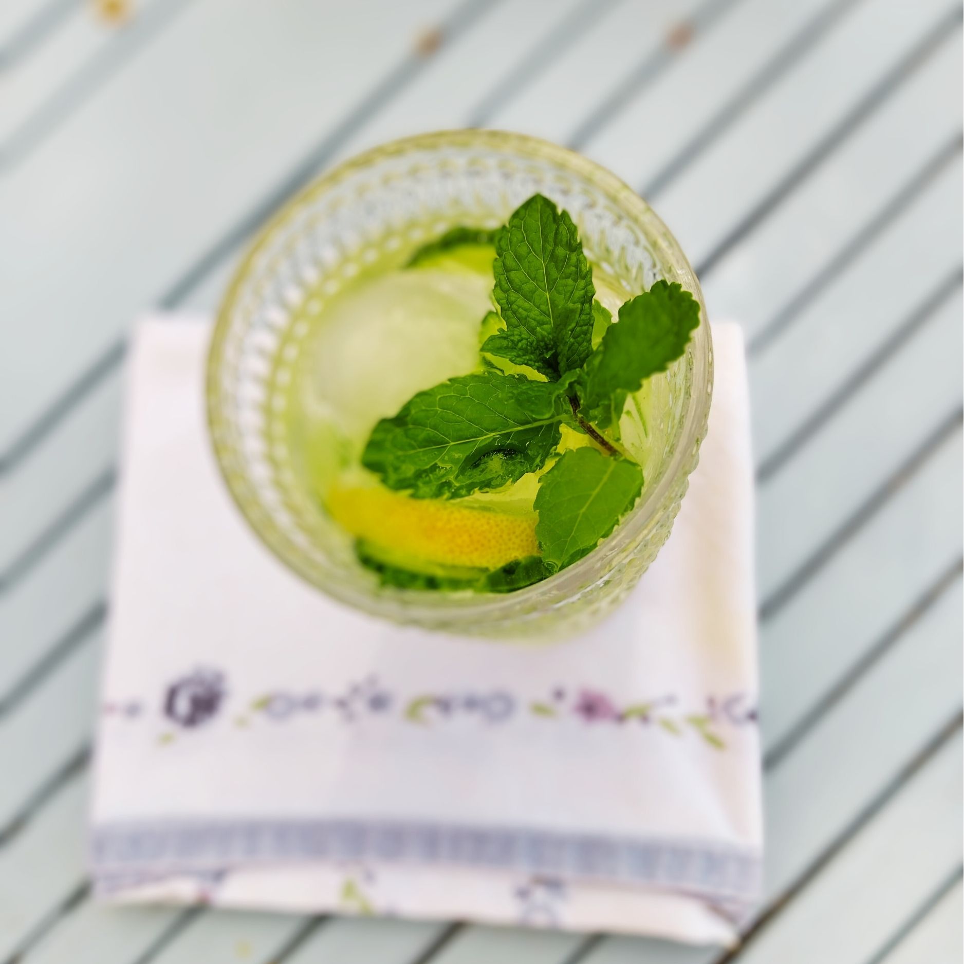 Birds eye view of Citron Presse in a glass with ice, lemon, cucumber and a sprig of mint